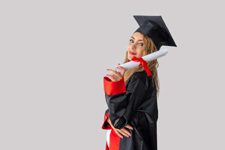 A pretty female student, celebrating her graduation and stand front of white wall holding her diploma with success. High quality photoの写真素材