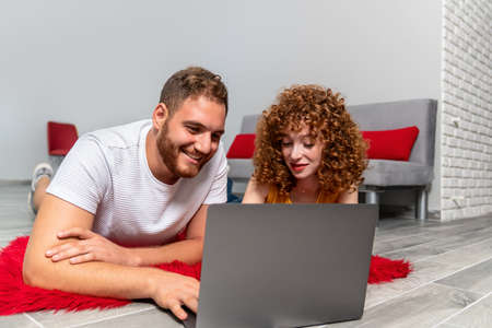 A Young couple lovers or friends laying on a red pluffy carpet and using laptop. High quality photoの写真素材