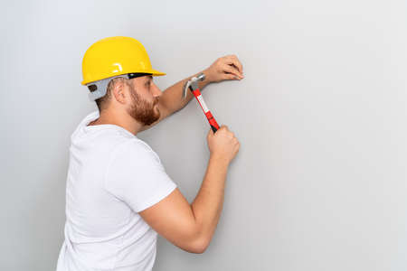 Young man worker is hitting the hammer to nail on the wall for construction or renovation. High quality photoの写真素材