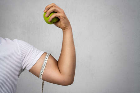 Young athletic man holding an apple and shows his biceps. Sport and diet for healthy life. High quality photoの写真素材