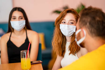 Grop of friends chatting and smiling while they sitting and drinking some beverage in a cafe with medical face mask.の写真素材