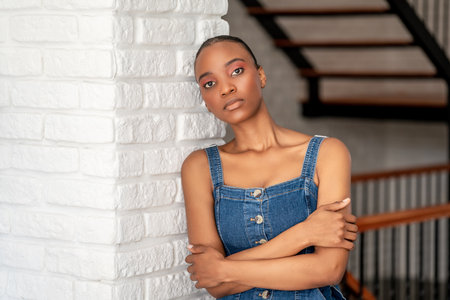 Young dark skin woman leans back on a white brick wall with crossed arms and looking to a point....