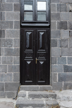 Old classical stone house with rustic, black, carved, vintage wooden door. Door textures and...