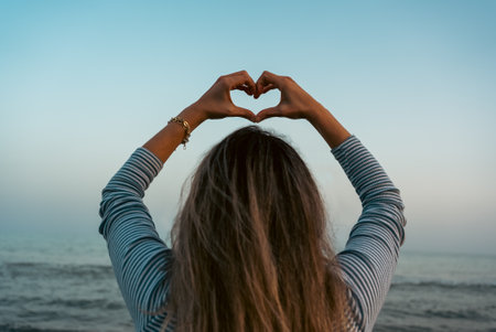 A woman makes a heart sign with her hands on the beach. High quality photoの写真素材