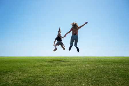 Happy mother and daughter jumping together on the grass. High quality photo