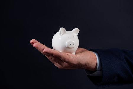 Piggy bank in businessman hand against black background. High quality photoの写真素材