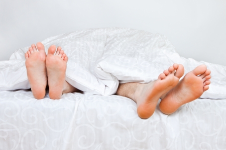 The bared heels of pair in stick out from under bed-sheetsの写真素材