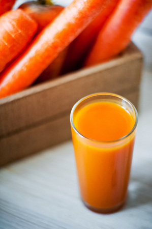 Photo of fresh carrots in a wooden box and a glass of freshly squeezed carrot juiceの写真素材