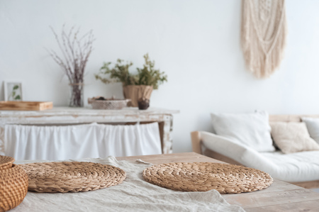 The white textured kitchen is blurred in the background in the style of shabby. A large table in an ecological style and loft style. Rustic napkins, wicker baskets, diyの写真素材