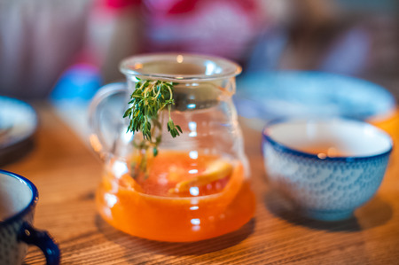 Summer tea in a large pot with a sprig. Tea with mango and orange on the table in a cafeの写真素材