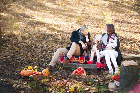 Autumn fashion for children and the whole family. Mom, Dad and two children on a picnic in autumn with apples, pumpkins. Family members have fun and laughsの写真素材