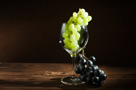 A bunch of green grapes and a glass of wine on a dark background. In a glass of grapesの写真素材