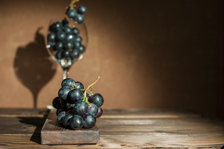 A bunch of blue dark grapes and a glass of wine on a dark background close up. In a glass of grapesの写真素材