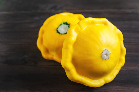 Beautiful picture of vegetables. Focus on two young patties squash. Patissons isolated on a dark wooden background close-up. Texture of vegetables is natural. Background and space for text on vegetablの写真素材