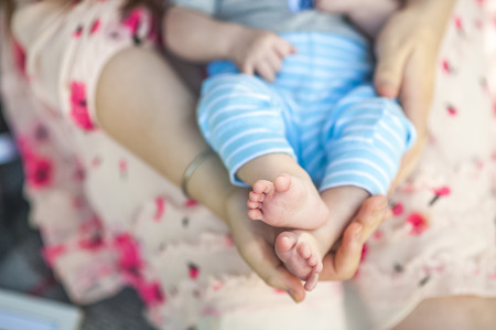 The concept of motherhood. The small legs of the baby are in the hands of the mother.の写真素材