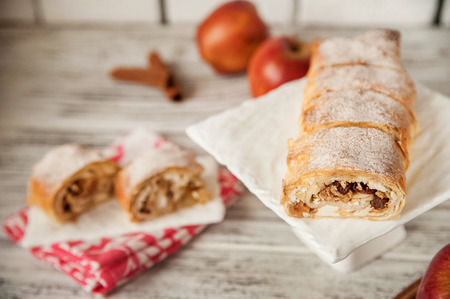 Apple strudel on a white square plate close-up and cut. Apple pie and red apples, cinnamon. Bright textural background with space for textの写真素材