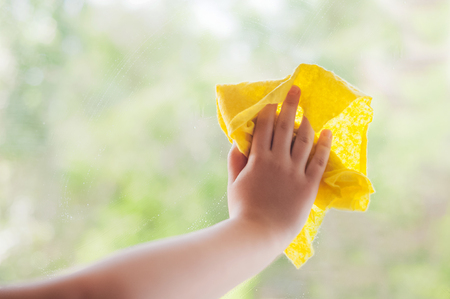 Children's hand close up with a yellow rag washes the windowの写真素材