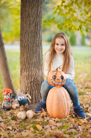 Little girl in green sweater on white background. The girl sits on pumpkins and laughs. Halloween conceptの写真素材
