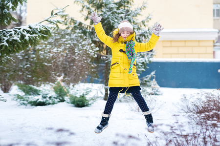 A girl in a yellow jacket in the winter rejoices in the snow Children's winter holidaysの写真素材