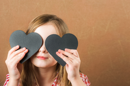 Girl and black slate heart. The girl builds a physiognomy, a grimaces and a heart for an inscription. Valentine's Day concept, close-up and copy spaceの写真素材