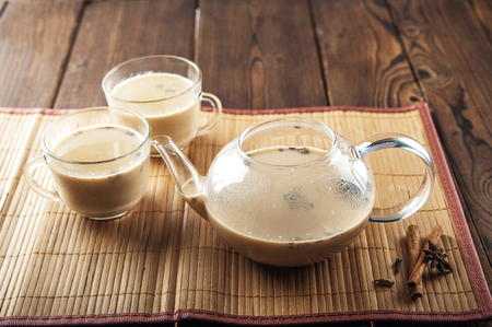 Masala tea on a textural wooden background. A teapot is a transparent cup of tea and Indian national tea masala. Milk, ginger, cardamom, cloves, nutmeg, star anise, cinnamonの写真素材