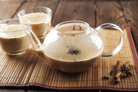 Masala tea on a textural wooden background. A teapot is a transparent cup of tea and Indian national tea masala. Milk, ginger, cardamom, cloves, nutmeg, star anise, cinnamonの写真素材