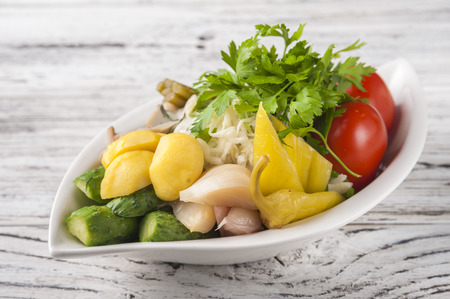 Fermented food on a white textural wooden table. Cucumbers, zucchini, garlic, marinade, tomatoes, cabbage, ramson, parsley. National Russian food pickles in brine close up and copy spaceの写真素材