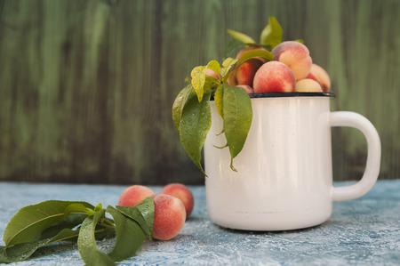 Homemade peaches with leaves in an enamelled white mug and copy space. Beautiful juicy ripe peaches.の写真素材