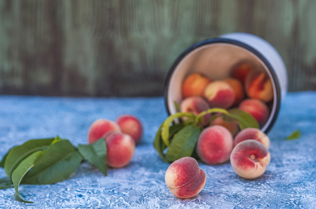 Homemade peaches with leaves in an enamelled white mug and copy space. Beautiful juicy ripe peaches.の写真素材