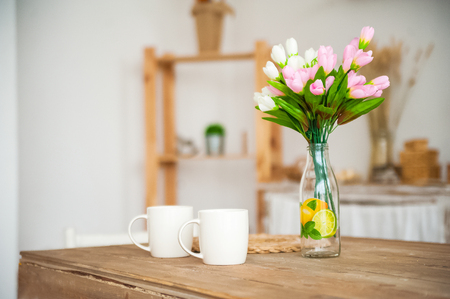 Breakfast cups and fruit. Spring tulips on the table. Wooden table in a bright rustic-style kitchen. Scandinavian style in the kitchen.の写真素材