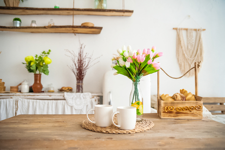 Breakfast cups and fruit. Spring tulips on the table. Wooden table in a bright rustic-style kitchen. Scandinavian style in the kitchen.の写真素材