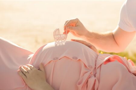 Male and female hands hold belly and closeup. Hands with a miniature strollerの写真素材