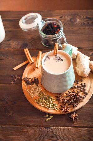 Details of still life in the home interior living room. Beautiful Cup of tea with milk, star anise, cinnamon on a wooden background. Cozy autumn-winter concept. Masala is a traditional hot spicy drink of the winter season with cinnamon, fennel, anise and other spices. Thanksgiving holiday celebration recipe. Flat lay.の写真素材