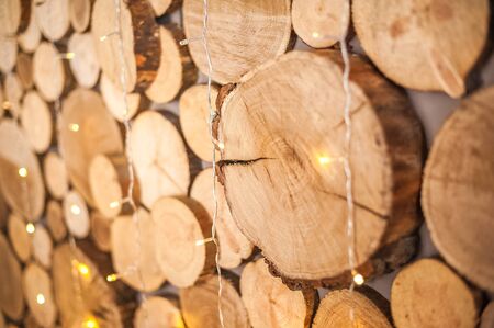 Background of natural wooden saw cuts and christmas garland. Christmas background made of wood and lights for text close-up and copy space.の写真素材