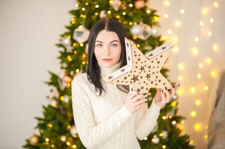 Lovely girl in the morning in a white knitted dress in the New Year's interior. Woman at home at Christmas time in a living room in a rustic style near a New Year tree.の写真素材