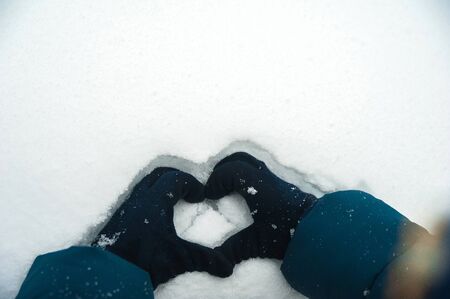 A child plays in the winter with snow. Hands holding a heart made of snow close-up and copy space.の写真素材