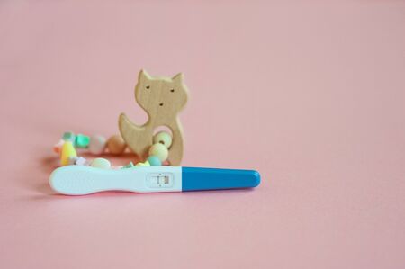 Wooden baby teether with beads and pregnancy test. Minimalistic flat lay with a wooden toys cat an isolated pink background. Toy for entertaining children and parents. Baby silicone teether with woodeの写真素材