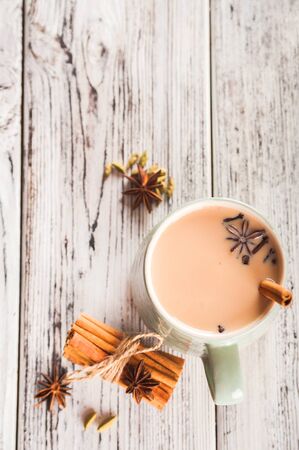 Clay cup on a wooden board on a light wooden table. A cup of masala tea. Spices cloves, fennel, cinnamon, cardamom, milk.の写真素材