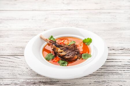 Vegetable soup with tomatoes in a restaurant close-up. Lamb soup on bone noodles on a white plate...