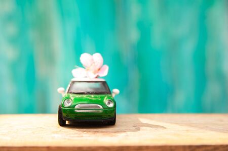 Floral background for text and a small car. Wooden table top with flowers close-up and copy space. Miniature car on a background of a blossoming tree in spring.の写真素材