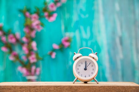 Floral background for text and a white clock. Wooden table top with flowers close-up and copy space. Alarm clock on a background of a blossoming tree in spring.の写真素材