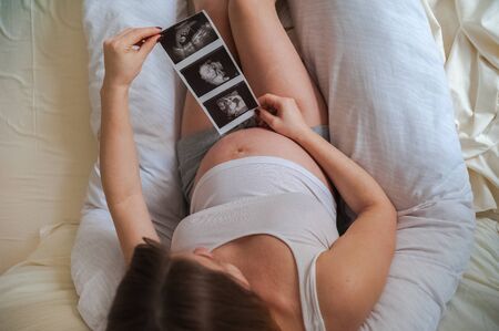 Pregnant woman with ultrasound picture of baby closeup. Snapshot of ultrasound and stomach. Pregnant on a pillow for pregnant women and copy space.の写真素材
