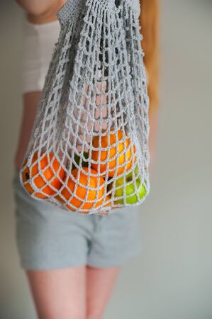 Pregnant and string bag with fruits. Healthy eating of a pregnant woman. Ecology and recycling with eco bag. mesh shopping bag in the hands of a pregnant woman closeup and copy space.の写真素材