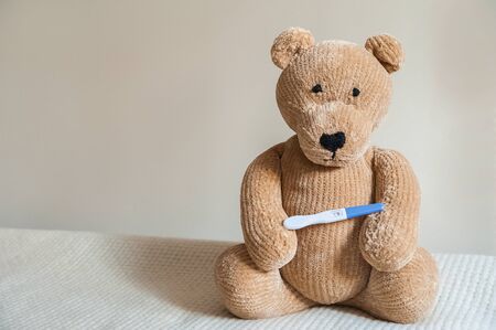 Teddy bear and positive pregnancy test close up and copy space. Children's toy bear, booties, test.の写真素材