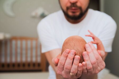 Father holds his head to the newborn. Small baby head in the hands of a parent close-up. Newborn baby care concept.の写真素材
