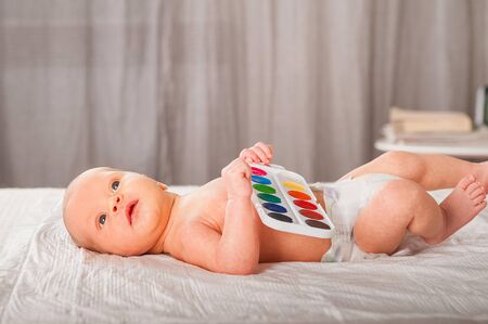 Newborn with paints on a white plaid closeup. Infant holds watercolor rainbow paint and copy space. The concept of the game, care and care for the baby.の写真素材