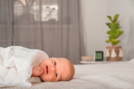 Newborn on the bed. Crying, screaming baby close up and copy space. Baby smile and colic in newborns. Seborrheic dermatitis in newbornsの写真素材