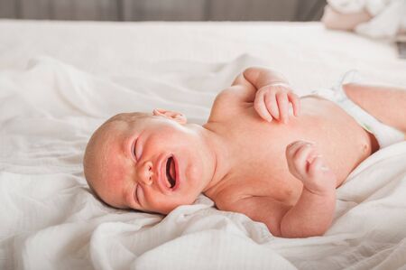 Newborn on the bed. Crying, screaming baby close up and copy space. Baby smile and colic in newborns. Seborrheic dermatitis in newbornsの写真素材