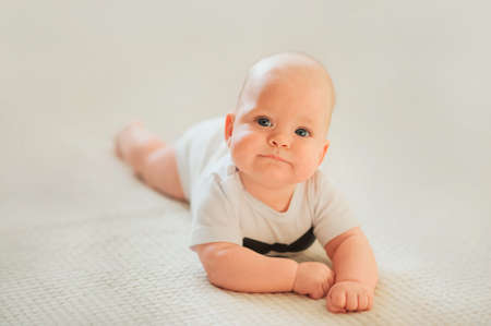 Newborn baby in white bodysuit and tie. Baby and copy space. Small child care, bathing, grimacing.