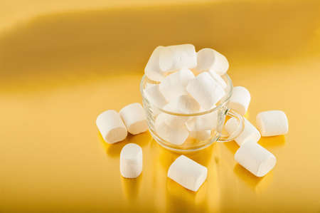 Marshmallows in a mug on a yellow background close-up and copy space. Marshmallow in a transparent mug on a gold background.の写真素材